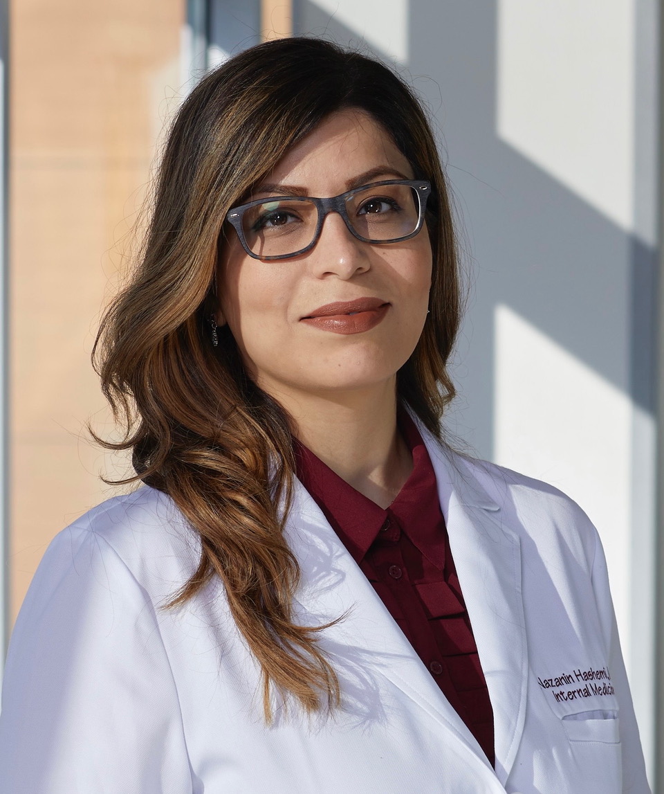 Doctor in white coat and glasses smiling.