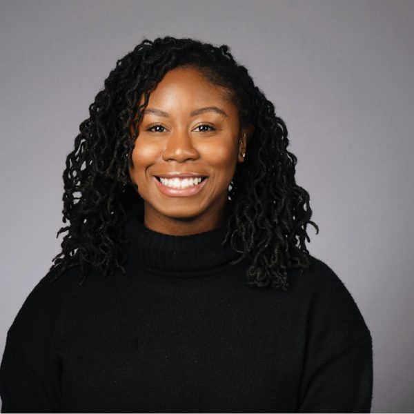 Person smiling with black sweater background gray.